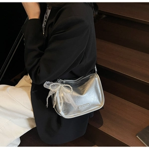 Close-up of silver crossbody bag featuring pearl bow detail and lace on a metal surface