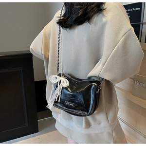 Detail view of black glossy pillow bag with lace bow and pearl chain on a sweater