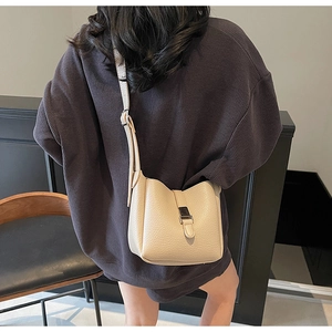 Detail of a beige lychee texture leather bucket bag with silver buckle worn on shoulder
