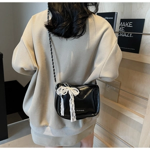 Detail of black soft leather crossbody bag with white lace and pearl bow decoration