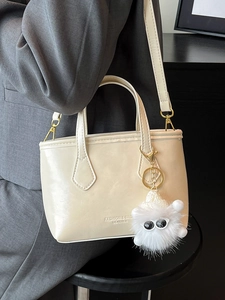 Minimalist beige PU leather bucket bag with plush charm shown worn as a crossbody