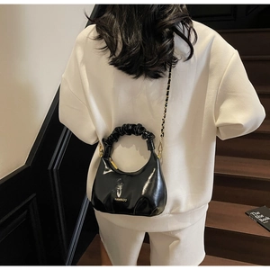 Détail d'un sac à main noir brillant plissé avec bandoulière chaîne tressée