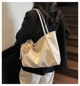 Close-up of white soft PU leather tote bag with a cute brown plush bear charm detail