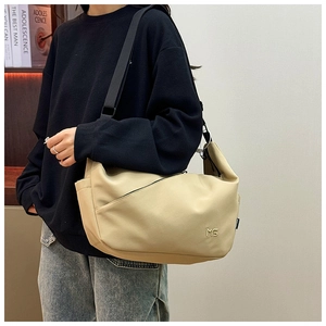 Detail view of large cream crossbody dumpling bag showing MS logo and wide strap on model