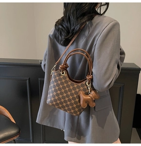 Détail du sac seau tendance avec motif vintage et breloque chien sur l'épaule du modèle