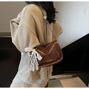 Detail of dark brown leather bag with white lace bow and pearl charms accessory