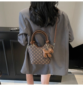 Détail d'un sac seau marron foncé avec charm chien porté sur une veste de blazer grise