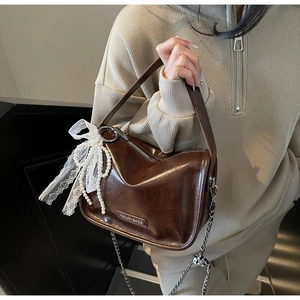 Detail of dark brown leather pillow bag featuring white lace bow and pearl charm