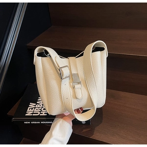 Detail of lychee textured cream leather bucket bag with silver metal buckle on wood