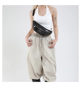 Close-up of black patent leather dumpling chest bag with shiny finish and silver zipper