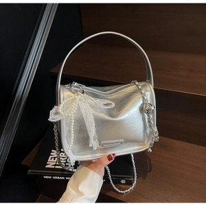 Detail of silver pillow bag featuring white lace, pearl bow, and metallic brand plaque