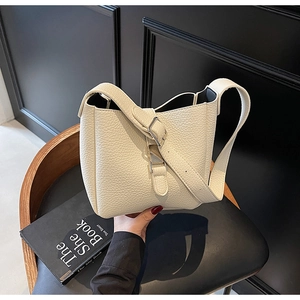 Close-up of off-white lychee grain leather bucket bag with adjustable wide strap and silver buckle