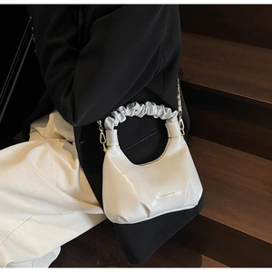 Détail du sac blanc avec poignée plissée, chaîne dorée et logo de marque gravé