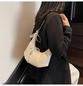 Detail shot of elegant beige hobo shoulder bag with lace bow and pearl heart charm.