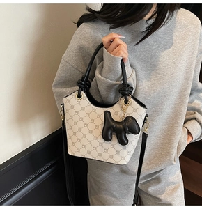 Détail du sac seau en cuir crème avec imprimé géométrique et breloque chiot