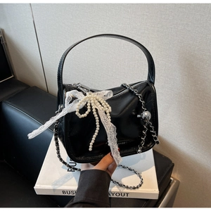 Detail of black soft leather pillow bag with elegant lace, pearl bow, and silver chain