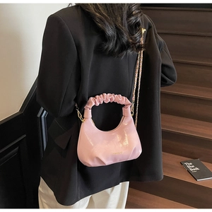 Détail d'un sac demi-lune rose avec poignée froncée et chaîne dorée porté à l'épaule