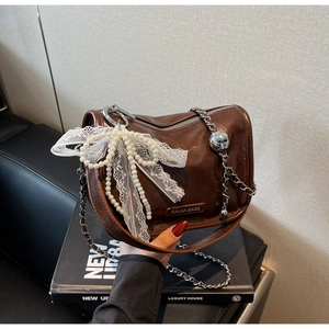 Detail of soft leather brown pillow bag with lace bow, pearl charm and chain strap