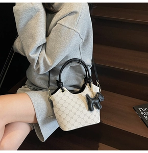 Vue détaillée du sac seau avec motif monogramme, poignée noire et breloque petit chien