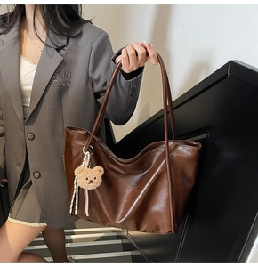 Detail of a large brown faux leather tote bag with slim straps and a cute plush bear charm