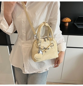 Détail du sac coquille jaune pâle, finition brillante, breloque cœur et chaîne