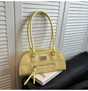 Détail d'un sac sous le bras en similicuir jaune pâle avec poche zippée et plaque en métal