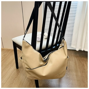 Close-up of the beige nylon hobo bag side pocket and metal MG logo on a wooden chair