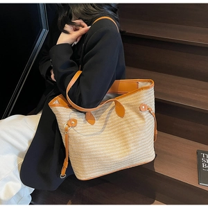 Detail view of woven straw tote bag with brown leather handles on dark wood steps