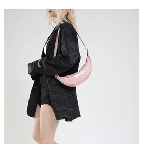 Close-up of pink crescent shoulder bag in matte leather worn by a model in a black suit