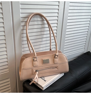 Détail du sac sous le bras beige avec plaque métal, fermeture à pompon et doubles lanières