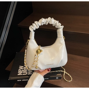 Détail du sac à main blanc avec poignée plissée, chaîne dorée et logo sur bois