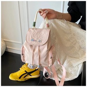 Detail of light pink backpack showing Mea Rey embroidery and decorative cord handles