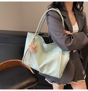 Detail of mint green soft leather tote bag with brown plush bear and striped ribbon charm