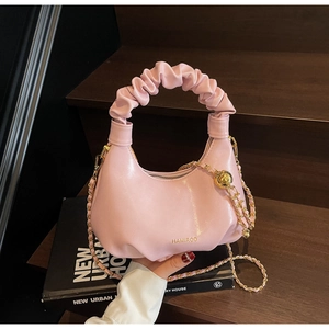 Détail d'un sac à main rose plissé avec bandoulière en chaîne dorée sur bois