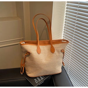 Detail view of woven straw tote bag with brown leather handles on a black sofa