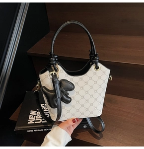 Détail du sac seau blanc imprimé avec garniture en cuir noir et breloque en forme de chiot