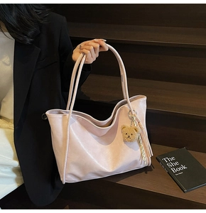 Detail of light pink faux leather tote bag with plush bear charm and tassel on stairs