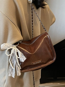 Deep brown leather crossbody pillow bag with silver chain strap shown on model shoulder