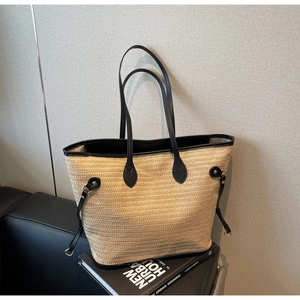 Close-up of contrast straw tote bag with black leather straps on modern design books