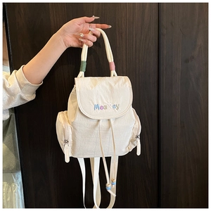 Detail of cream white mini backpack showing drawstring closure and brand embroidery