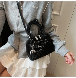Détail d'un sac coquillage en cuir verni noir avec clous et breloque cœur en chaîne