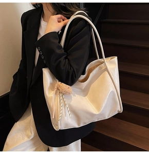 Side view of cream beige faux leather tote bag with brown plush ball charm on shoulder