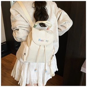 Detail view of cream canvas mini backpack with colorful embroidery and woven top handle