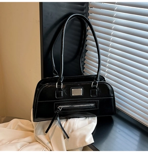 Gros plan détaillé du sac bandoulière en cuir verni noir brillant avec plaque argentée