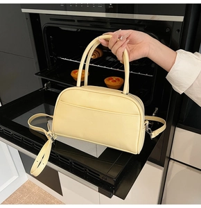 Detail of butter yellow faux leather pillow bag featuring silver zipper and front pocket