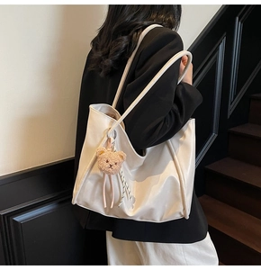 Close-up of white leather tote bag featuring a cute brown plush bear charm and long straps