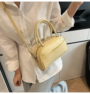 Close-up of a light yellow pillow bag with double zippers and adjustable strap on a model