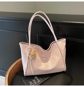 Detail view of pink large capacity tote bag with bear charm on black leather stool