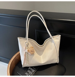 Detail of off-white tote bag with soft leather texture and plush bear pendant