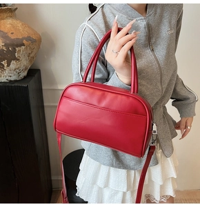 Red leather Boston bag detail showing hand-held style and adjustable shoulder strap on model